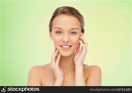 beauty, people and health concept - smiling young woman with bare shoulders touching her face over green natural background