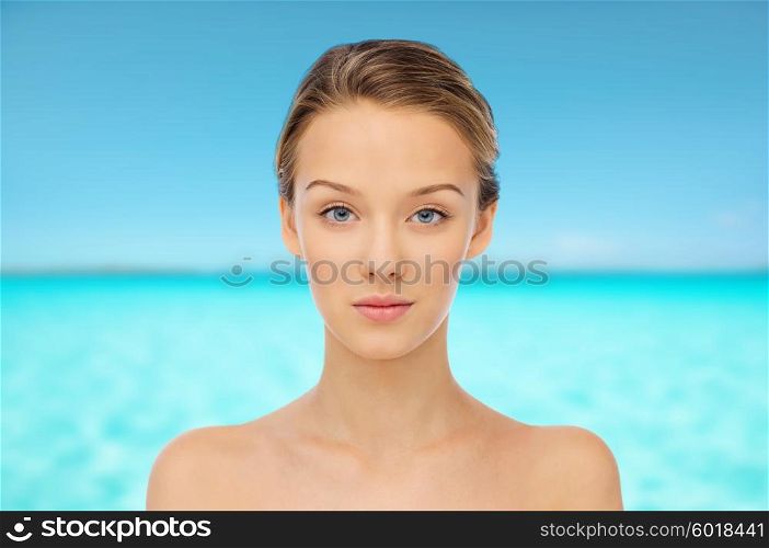 beauty, people and health concept - young woman face and shoulders over blue sea and sky background