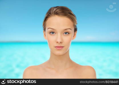 beauty, people and health concept - young woman face and shoulders over blue sea and sky background