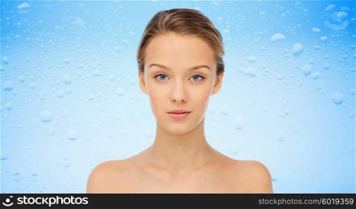 beauty, people and health concept - young woman face and shoulders over water drops on blue background
