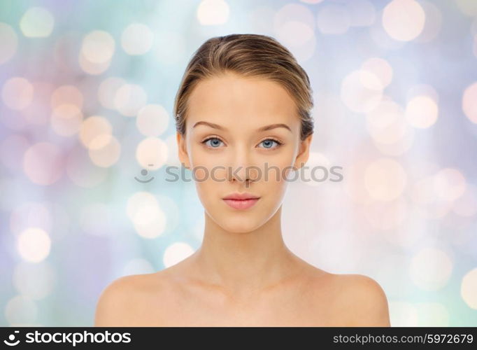 beauty, people and health concept - young woman face and shoulders over blue holidays lights background