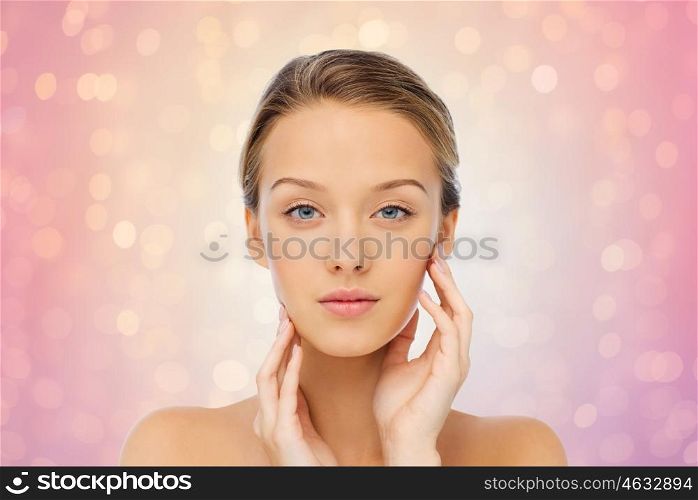 beauty, people and health concept - young woman with bare shoulders touching her face over rose quartz and serenity lights background