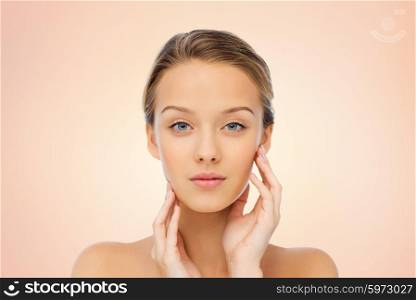 beauty, people and health concept - young woman with bare shoulders touching her face over beige background
