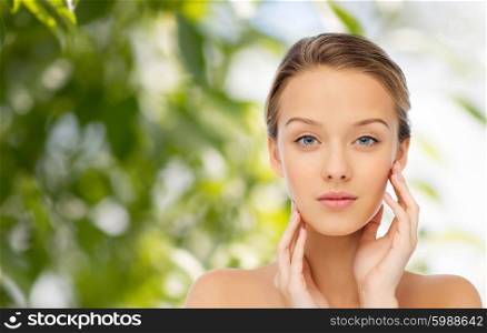 beauty, people and health concept - young woman with bare shoulders touching her face over green natural background