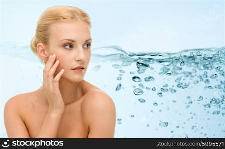 beauty, people and health concept - young woman with bare shoulders touching her face over water splash on blue background