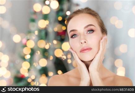 beauty, people and holidays concept - beautiful young woman face and hands over christmas tree lights background