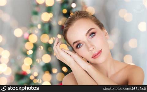 beauty, people and holidays concept - beautiful young woman face and hands over christmas tree lights background