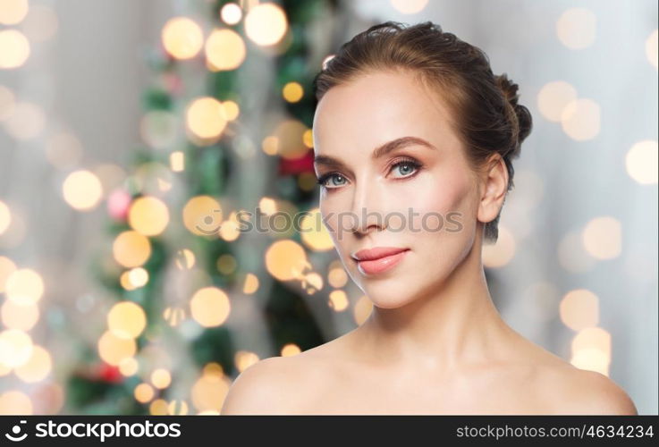 beauty, people and holidays concept - beautiful young woman face over christmas tree lights background
