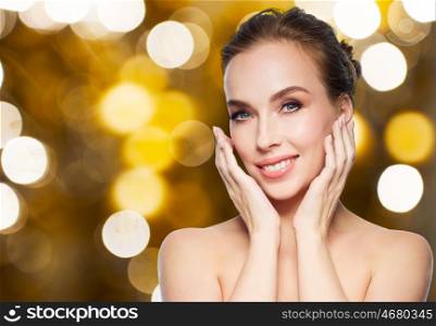 beauty, people and holidays concept - beautiful young woman touching her face over lights background