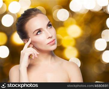 beauty, people and holidays concept - beautiful young woman touching her face over lights background