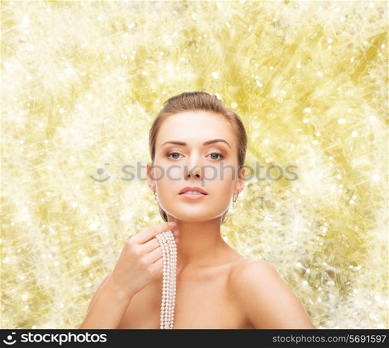 beauty, people and jewelery concept - beautiful woman with pearl earrings and necklace over yellow lights background