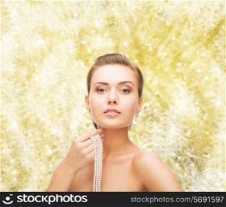 beauty, people and jewelery concept - beautiful woman with pearl earrings and necklace over yellow lights background