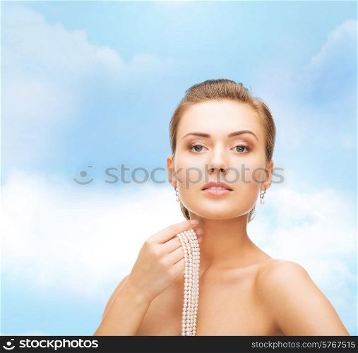 beauty, people and jewelry concept - beautiful woman with pearl earrings and necklace over blue cloudy sky background