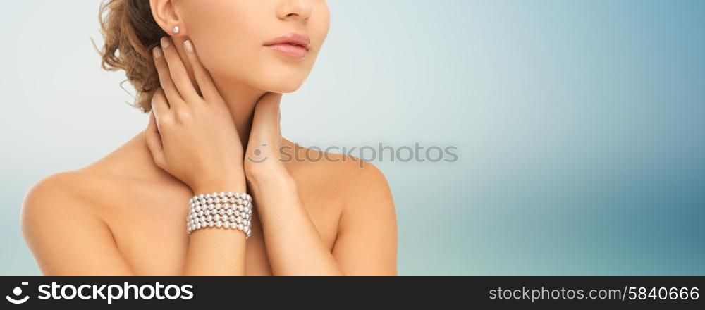 beauty, people and jewelry concept - close up of beautiful woman with pearl earrings and bracelet over blue background