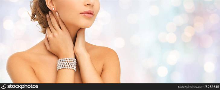 beauty, people and jewelry concept - close up of beautiful woman with pearl earrings and bracelet over blue holidays lights background
