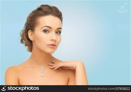 beauty, people and jewelry concept - woman wearing shiny diamond pendant over blue background