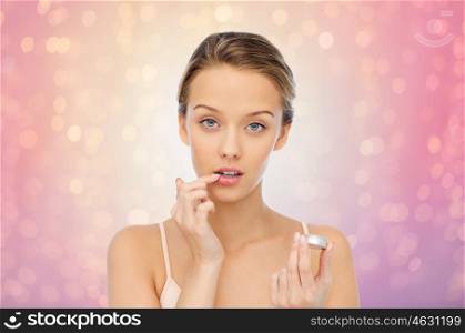 beauty, people and lip care concept - young woman applying lip balm to her lips over rose quartz and serenity lights background