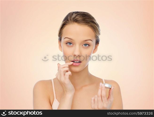 beauty, people and lip care concept - young woman applying lip balm to her lips over beige background