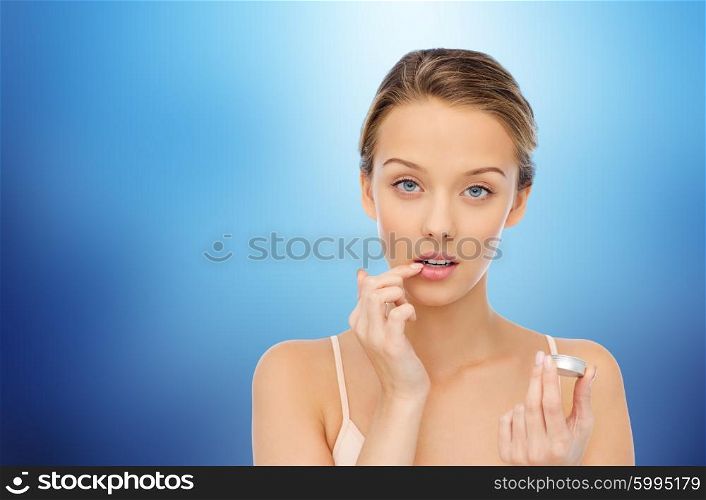 beauty, people and lip care concept - young woman applying lip balm to her lips over marine blue background