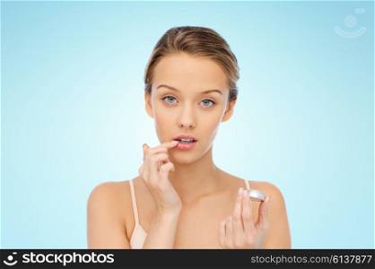 beauty, people and lip care concept - young woman applying lip balm to her lips over blue background