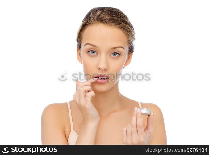 beauty, people and lip care concept - young woman applying lip balm to her lips