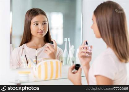 beauty, people and make up concept - teenage girl spraying perfume at home bathroom. teenage girl spraying perfume at bathroom