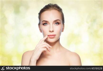 beauty, people and plastic surgery concept - beautiful young woman showing her lips over yellow holidays lights background