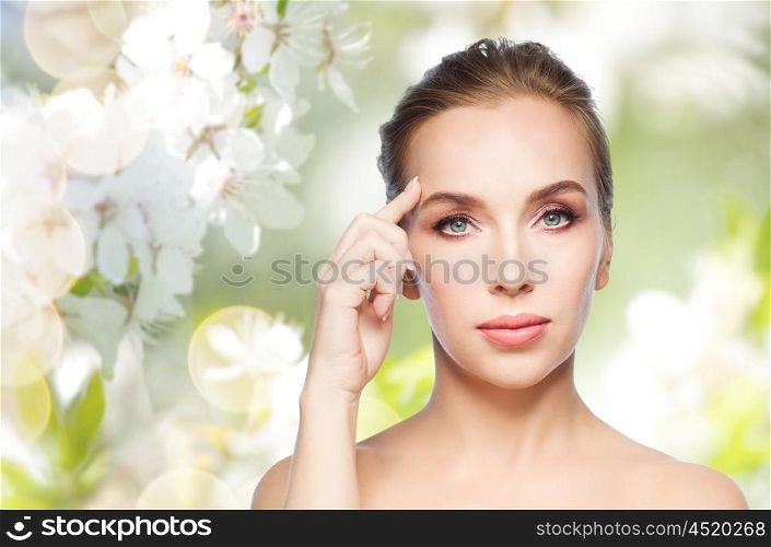beauty, people and plastic surgery concept - beautiful young woman showing her forehead over natural spring cherry blossom background