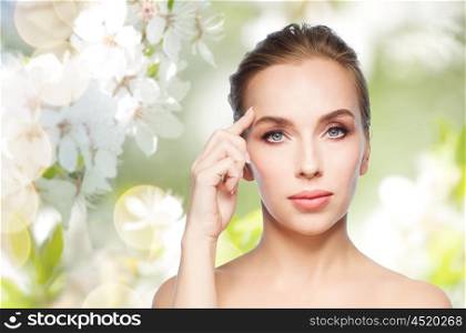 beauty, people and plastic surgery concept - beautiful young woman showing her forehead over natural spring cherry blossom background