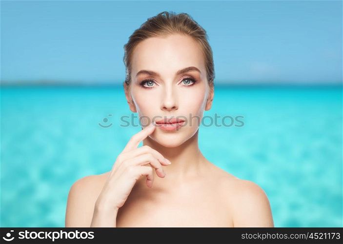 beauty, people and plastic surgery concept - beautiful young woman showing her lips over blue sea and sky background