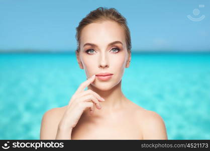 beauty, people and plastic surgery concept - beautiful young woman showing her lips over blue sea and sky background