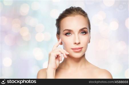 beauty, people and plastic surgery concept - beautiful young woman showing her cheekbone over blue holidays lights background