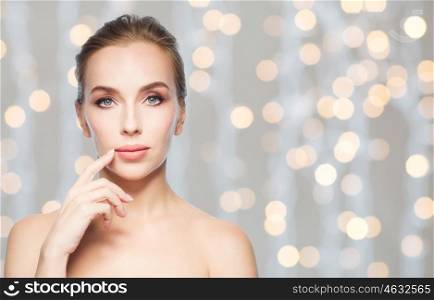 beauty, people and plastic surgery concept - beautiful young woman showing her lips over holidays lights background