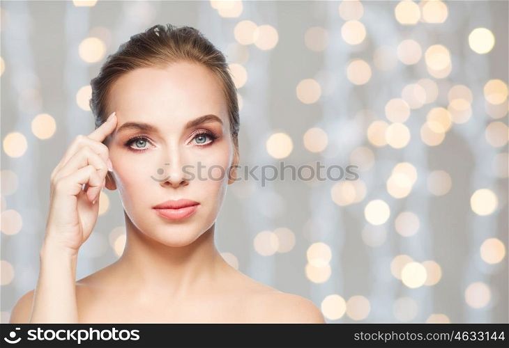 beauty, people and plastic surgery concept - beautiful young woman showing her forehead over holidays lights background
