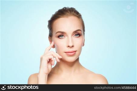 beauty, people and plastic surgery concept - beautiful young woman showing her cheekbone over blue background