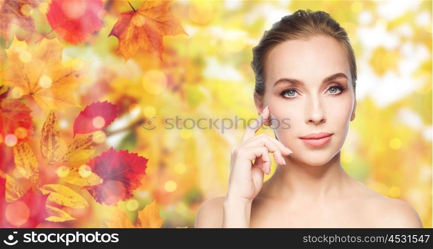 beauty, people and skin care concept - beautiful young woman showing her cheekbone over natural autumn leaves and lights background