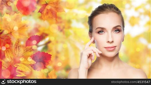beauty, people and skin care concept - beautiful young woman showing her cheekbone over natural autumn leaves and lights background