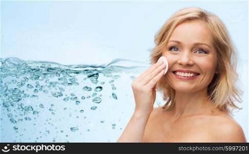 beauty, people and skincare concept - happy middle aged woman cleaning face and removing make up with cotton pad over water splash with air bubbles background