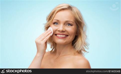 beauty, people and skincare concept - happy middle aged woman cleaning face and removing make up with cotton pad over blue background