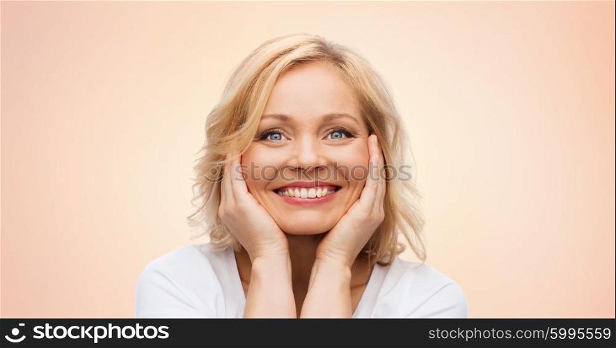 beauty, people and skincare concept - smiling middle aged woman in white shirt touching face over beige background