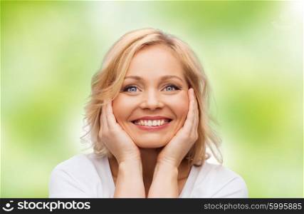 beauty, people and skincare concept - smiling middle aged woman in white shirt touching face over green natural background
