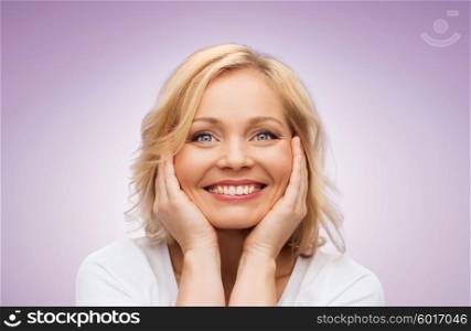 beauty, people and skincare concept - smiling middle aged woman in white shirt touching face over violet background