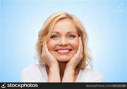 beauty, people and skincare concept - smiling middle aged woman in white shirt touching face over blue background