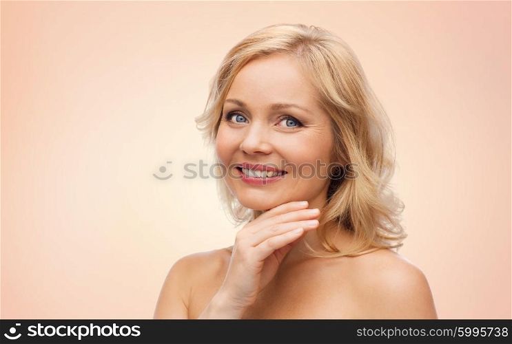 beauty, people and skincare concept - smiling middle aged woman with bare shoulders touching face over beige background