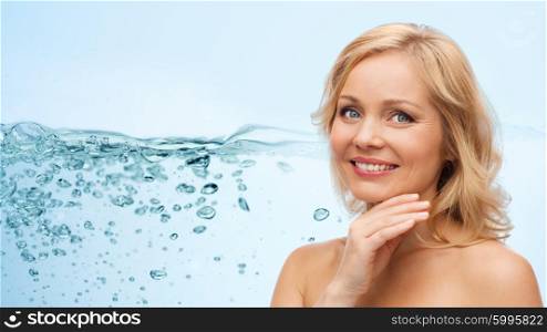 beauty, people and skincare concept - smiling middle aged woman with bare shoulders touching face over water splash with air bubbles background
