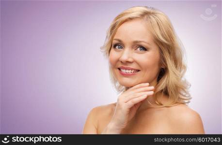 beauty, people and skincare concept - smiling middle aged woman with bare shoulders touching face over violet background