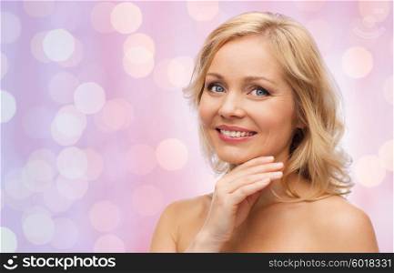 beauty, people and skincare concept - smiling middle aged woman with bare shoulders touching face over pink holidays lights background