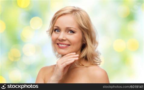 beauty, people and skincare concept - smiling middle aged woman with bare shoulders touching face over green holidays lights background