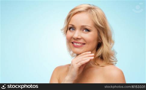 beauty, people and skincare concept - smiling middle aged woman with bare shoulders touching face over blue background