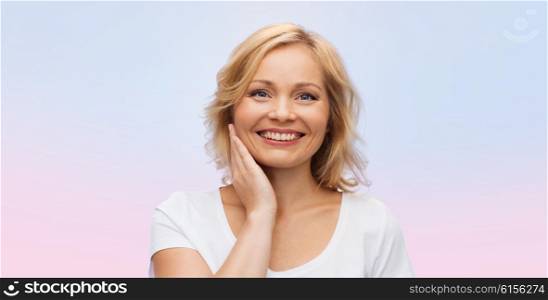 beauty, people and skincare concept - smiling woman in white shirt touching face over rose quartz and serenity gradient background